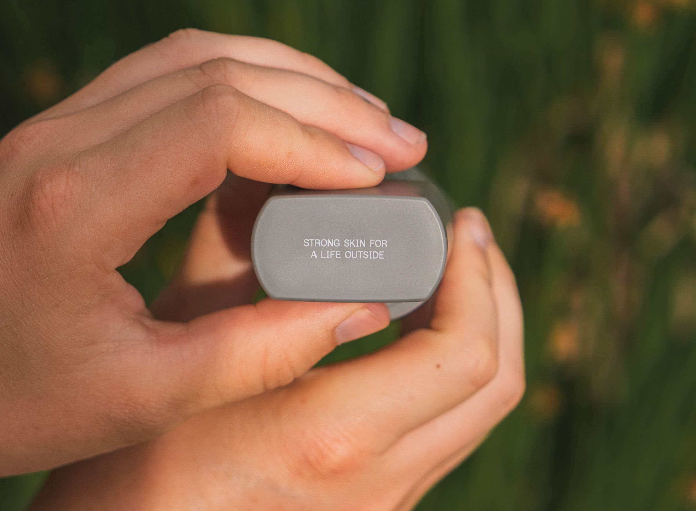Hands hold a small gray sunscreen tube reading Strong Skin For A Life Outside.